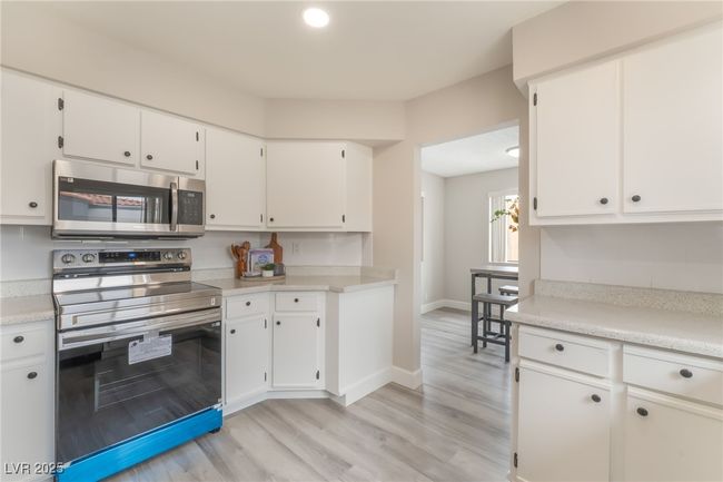 Kitchen with stainless steel appliances, light countertops, white cabinetry, and light wood-style flooring | Image 10