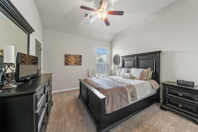 This bedroom features a vaulted ceiling with a ceiling fan, neutral walls, and carpeted flooring. A window allows for natural light, enhancing the room's spacious feel. | Image 24