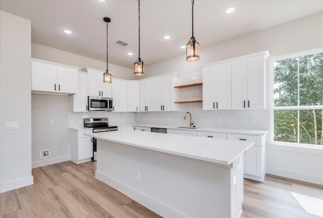 Kitchen featuring appliances with stainless steel finishes, open shelves, a center island, backsplash, and light countertops | Image 9