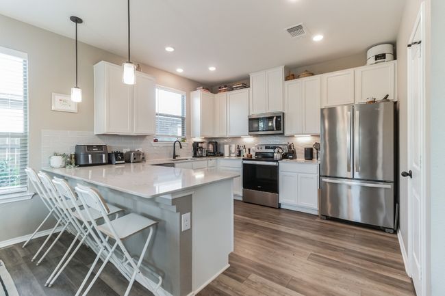 Kitchen featuring appliances with stainless steel finishes, a peninsula, wood finished floors, white cabinetry, and recessed lighting | Image 11