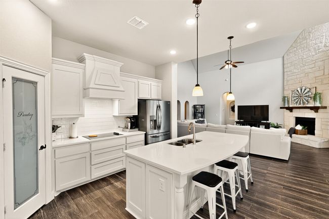 Kitchen with a sink, stainless steel fridge, decorative backsplash, black electric cooktop, and custom exhaust hood | Image 9