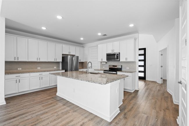 Kitchen featuring white cabinets, wood finished floors, stainless steel appliances, a center island with sink, and a sink | Image 15