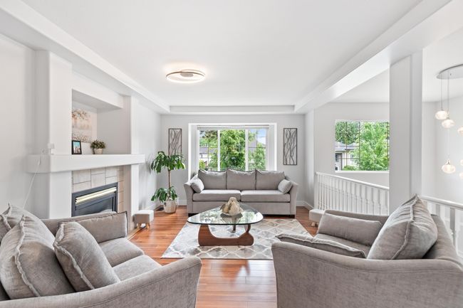 Living room with wood finished floors, a fireplace, a tray ceiling, and baseboards | Image 4