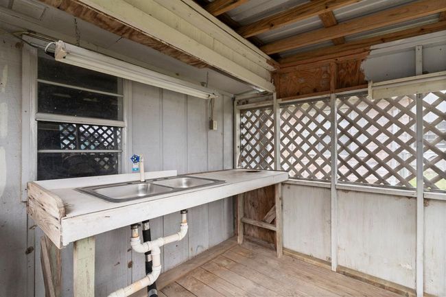 Outdoor utility area with a double sink, wooden lattice walls, and exposed beams. It's a functional space that may be used for gardening or cleaning tasks. | Image 31