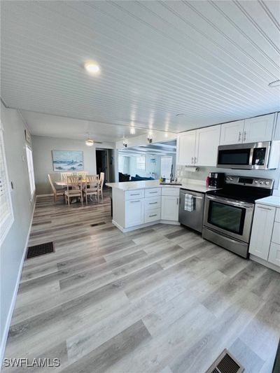 Kitchen with kitchen peninsula, appliances with stainless steel finishes, white cabinets, and light hardwood / wood-style floors | Image 3