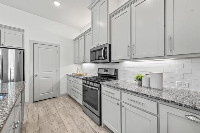 Kitchen featuring decorative backsplash, light wood-type flooring, light stone countertops, and appliances with stainless steel finishes | Image 18