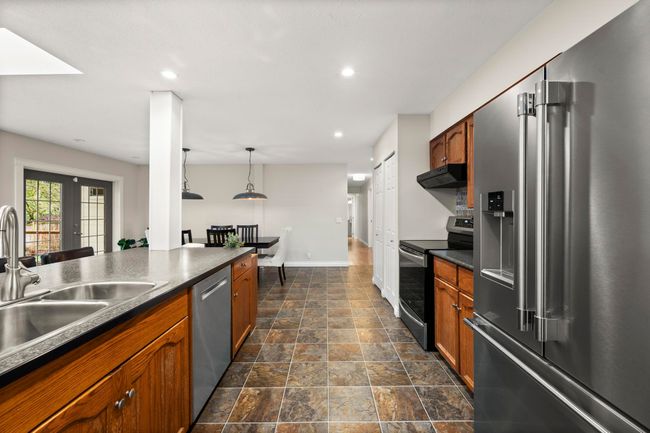 Kitchen featuring appliances with stainless steel finishes, under cabinet range hood, a sink, dark countertops, and brown cabinets | Image 13
