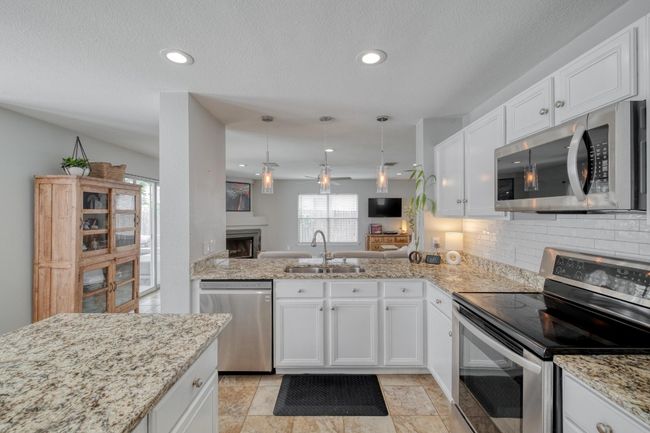 Kitchen with appliances with stainless steel finishes, decorative backsplash, white cabinets, light stone countertops, and recessed lighting | Image 7