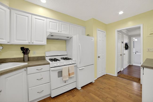 Kitchen featuring white appliances, under cabinet range hood, white cabinets, light wood finished floors, and recessed lighting | Image 14
