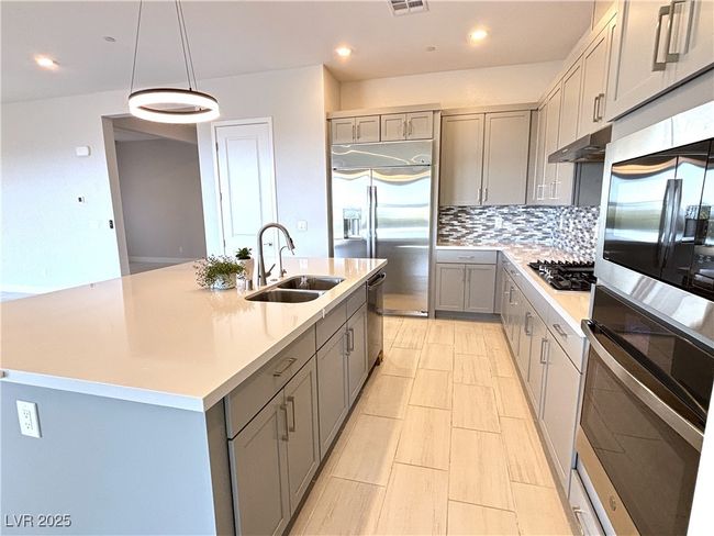 Kitchen with gray cabinets, stainless steel appliances, light countertops, and a sink | Image 12