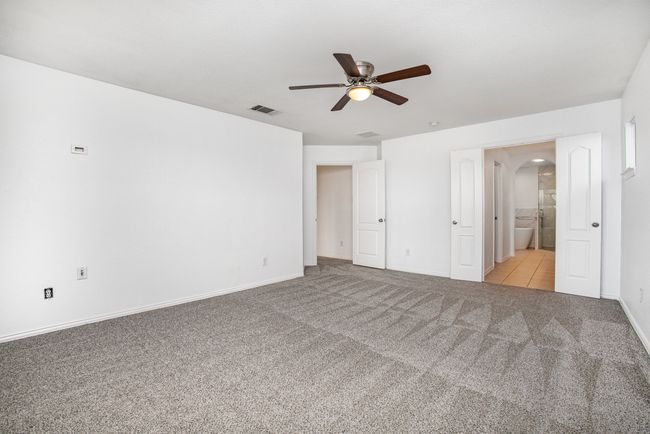 Unfurnished bedroom with connected bathroom, baseboards, visible vents, arched walkways, and carpet | Image 20