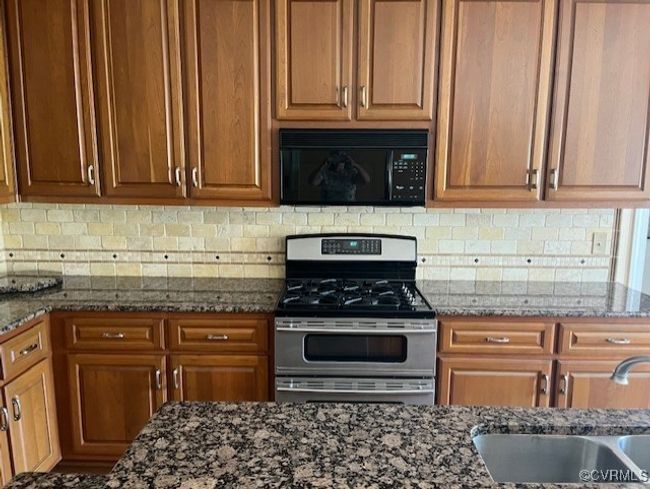 Kitchen with gas range, black microwave, decorative backsplash, dark stone countertops, and brown cabinetry | Image 5