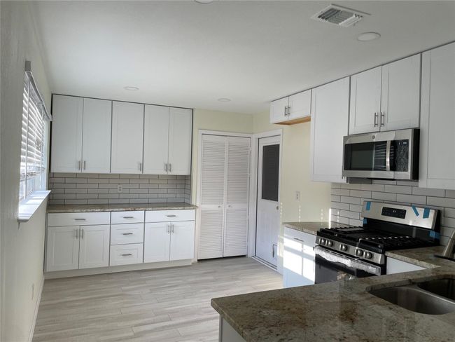 Kitchen featuring appliances with stainless steel finishes, stone counters, backsplash, and white cabinets | Image 15