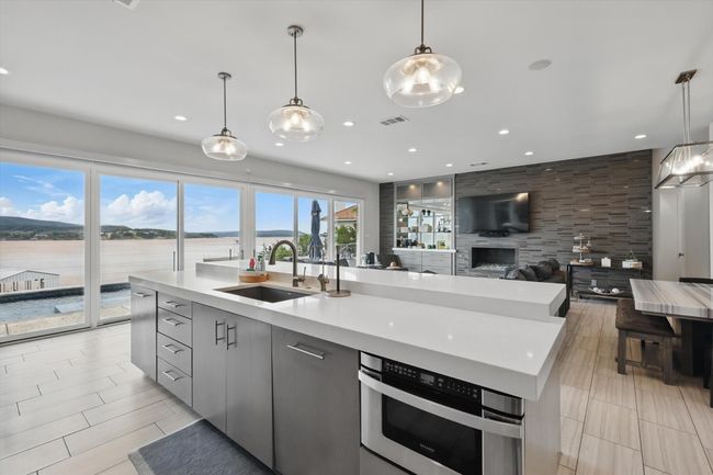 Kitchen with modern cabinets, hanging light fixtures, a center island with sink, a sink, and light countertops | Image 20