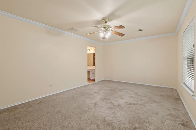 The oversized primary bedroom features carpet, crown molding, ceiling fan and large picture windows. | Image 13