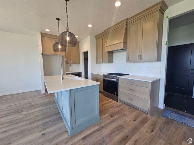 Kitchen with stainless steel range with gas cooktop, custom range hood, light wood-type flooring, a sink, and recessed lighting | Image 4