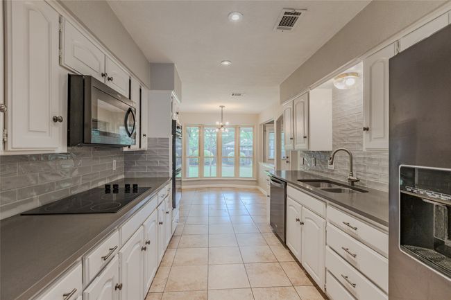 Kitchen with black appliances, dark countertops, white cabinetry, backsplash, and a chandelier | Image 9