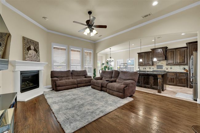 Living area with a chandelier, a glass covered fireplace, dark wood-type flooring, ornamental molding, and ceiling fan | Image 15