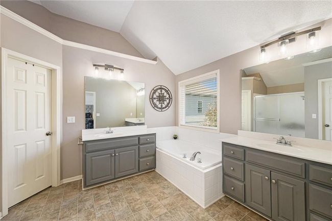 Bathroom with a bath, a shower stall, two vanities, vaulted ceiling, and baseboards | Image 31