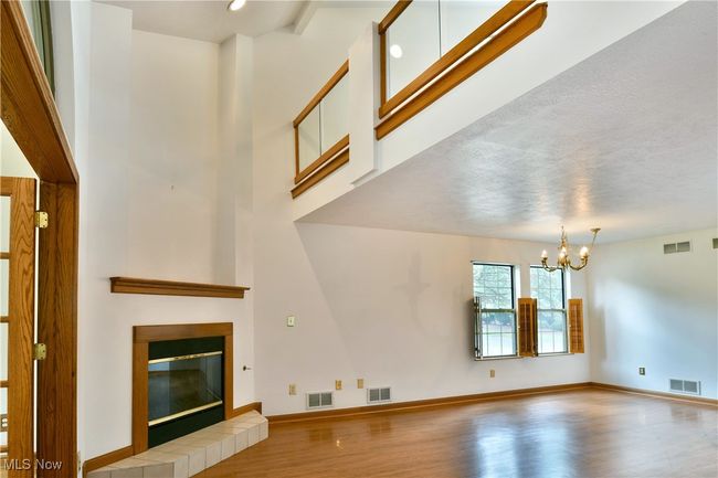 Unfurnished living room featuring wood finished floors, a chandelier, a fireplace, and a high ceiling | Image 18