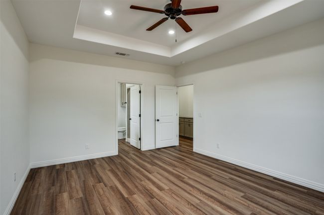 Spare room featuring dark wood-style flooring, baseboards, visible vents, ceiling fan, and a raised ceiling | Image 15