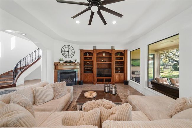 The living room sits on the back of the home with a high ceiling, recessed lighting, ceiling speaker pre-wiring and beautiful tile floors. Included is a built-in entertainment center and a corner gas log fireplace with a handcrafted solid pine mantel, granite surround & hearth. | Image 8
