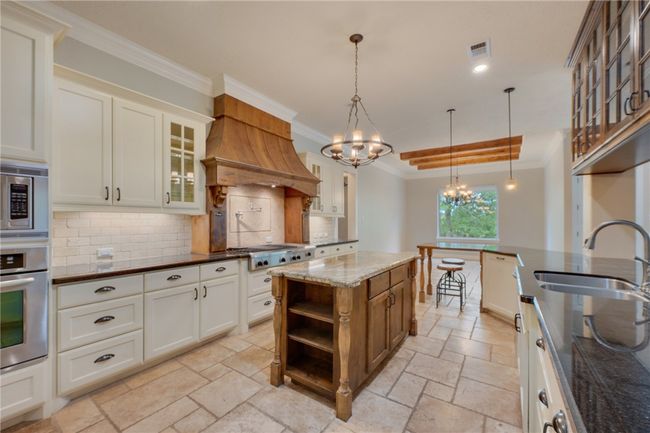 Kitchen featuring a sink, stone tile floors, a chandelier, ornamental molding, and stainless steel appliances | Image 8