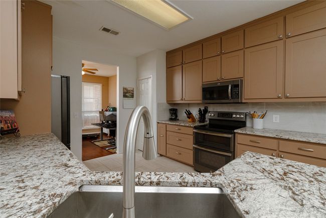 Kitchen with a sink, light stone countertops, appliances with stainless steel finishes, visible vents, and decorative backsplash | Image 12