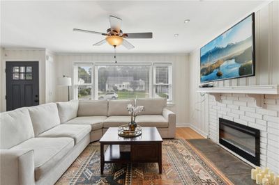 Living room with wood-type flooring, a brick fireplace, and ceiling fan | Image 3