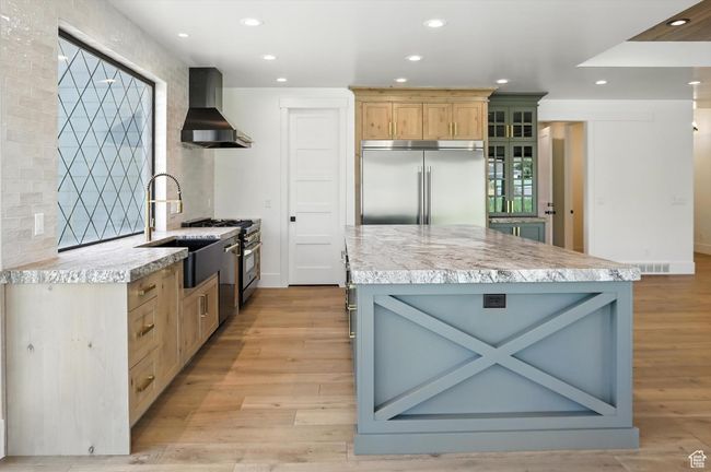 Kitchen with wall chimney range hood, premium appliances, light countertops, light wood-style flooring, and recessed lighting | Image 14