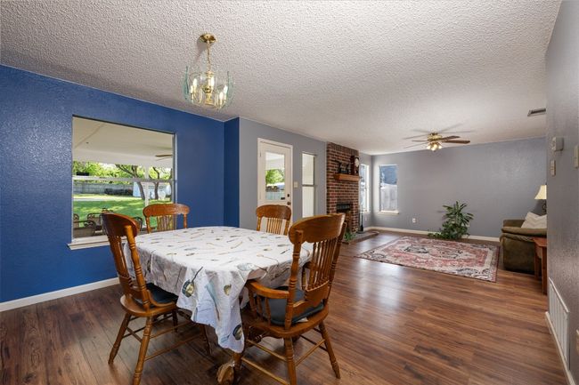 Dining room featuring baseboards, a fireplace, a textured ceiling, wood finished floors, and ceiling fan with notable chandelier | Image 12