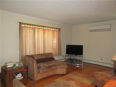 Living room with a baseboard heating unit, a wall mounted AC, wood-type flooring, and crown molding | Image 2