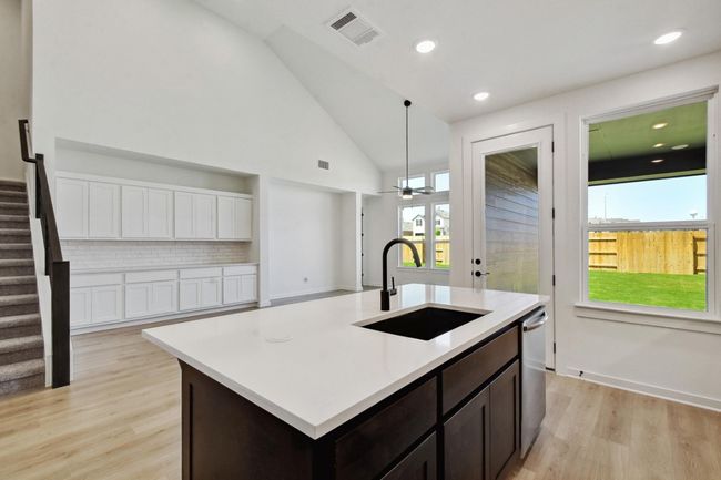 Kitchen with decorative backsplash, dark brown cabinets, light wood-type flooring, a center island with sink, and recessed lighting | Image 8