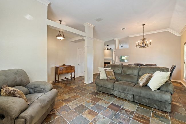 Living room featuring stone tile flooring, crown molding, baseboards, a warm lit fireplace, and lofted ceiling | Image 5