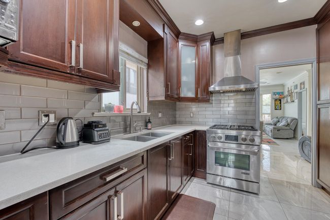 Kitchen featuring designer stove, wall chimney range hood, light marble finish floors, ornamental molding, and tasteful backsplash | Image 11