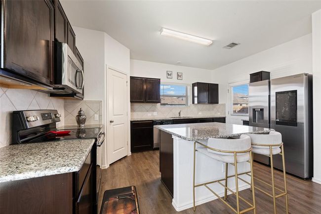 Kitchen featuring appliances with stainless steel finishes, a sink, dark brown cabinets, a breakfast bar area, and light stone counters | Image 7