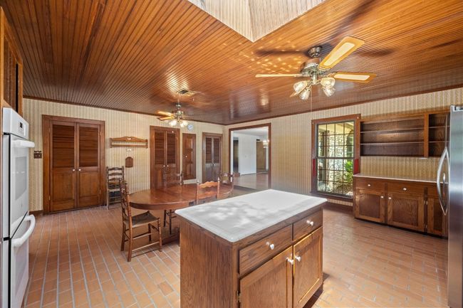 Kitchen featuring freestanding refrigerator, ceiling fan, wallpapered walls, and brick flooring | Image 13