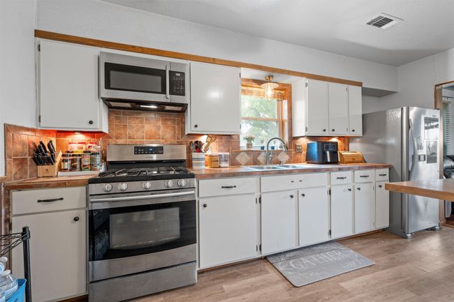Kitchen with a sink, appliances with stainless steel finishes, light wood-style flooring, visible vents, and white cabinets | Image 6