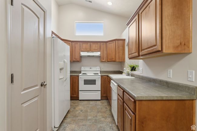 Kitchen with under cabinet range hood, white appliances, a sink, brown cabinets, and high vaulted ceiling | Image 15