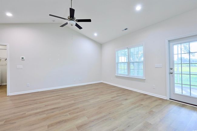 Empty room with healthy amount of natural light, light wood-style floors, lofted ceiling, a ceiling fan, and recessed lighting | Image 4