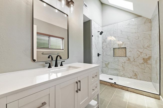Bathroom with walk in shower, vanity, a skylight, a textured wall, and tile patterned floors | Image 7