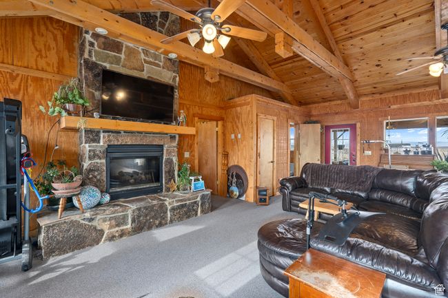 Carpeted living room featuring ceiling fan, wooden ceiling, beamed ceiling, a stone fireplace, and wood walls | Image 24