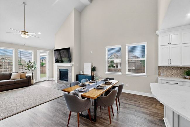 Dining area featuring dark wood-type flooring, high vaulted ceiling, a glass covered fireplace, plenty of natural light, and a ceiling fan | Image 4