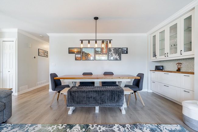 Dining room with light wood grain laminate flooring, crown molding, and baseboards | Image 4
