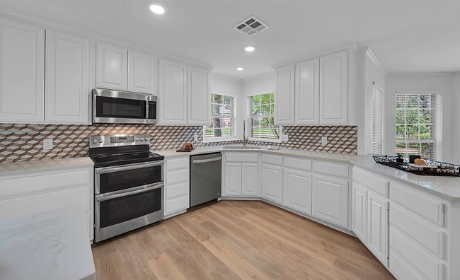Kitchen with stainless steel appliances, a sink, visible vents, light wood-style floors, and white cabinetry | Image 11