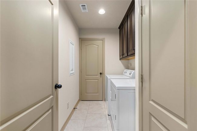 Laundry room with light tile patterned floors, washing machine and dryer, visible vents, baseboards, and cabinet space | Image 20