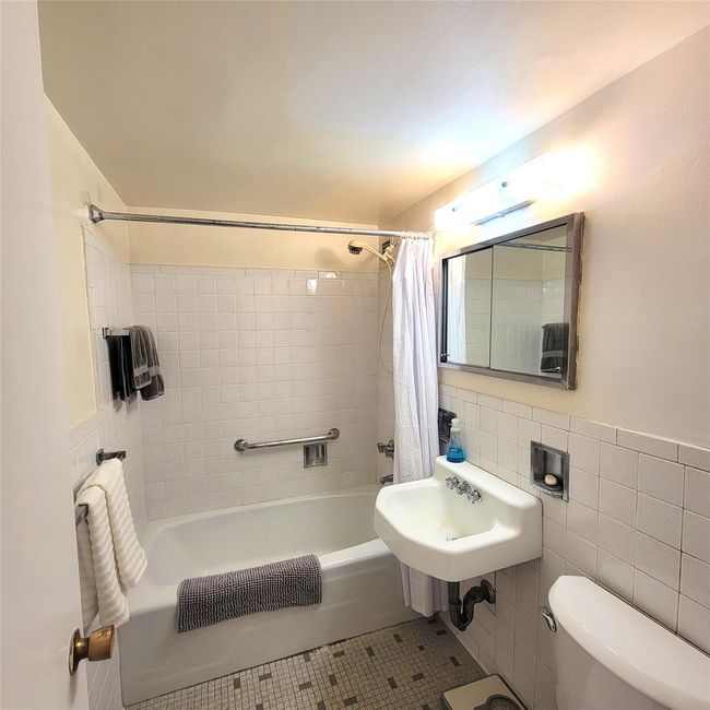 Bathroom with shower / bath combination with curtain, toilet, tile walls, a sink, and tile patterned floors | Image 8