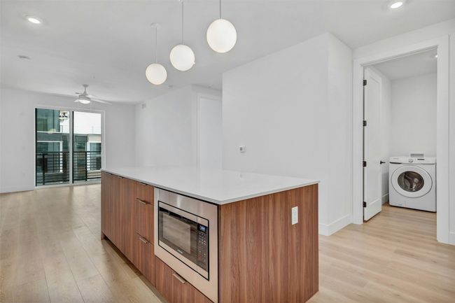 Kitchen featuring washer / dryer, modern cabinets, stainless steel microwave, brown cabinets, and light wood-style flooring | Image 6