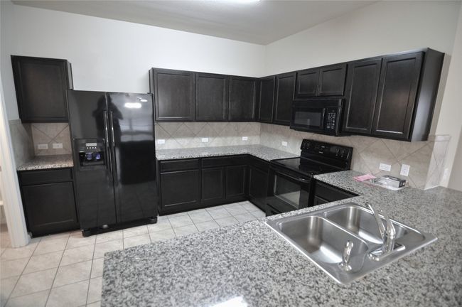 Kitchen featuring a sink, decorative backsplash, light tile patterned floors, black appliances, and dark cabinets | Image 13