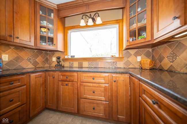 Kitchen features Granite countertop, decorative backsplash, and cabinet glass inserts. | Image 12